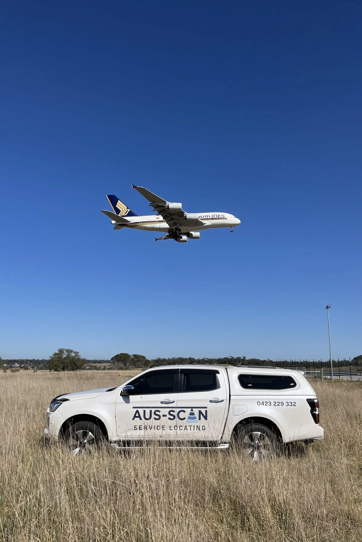 The Aus-Scan Service Locating ute parked in a grassy field under a passing plane