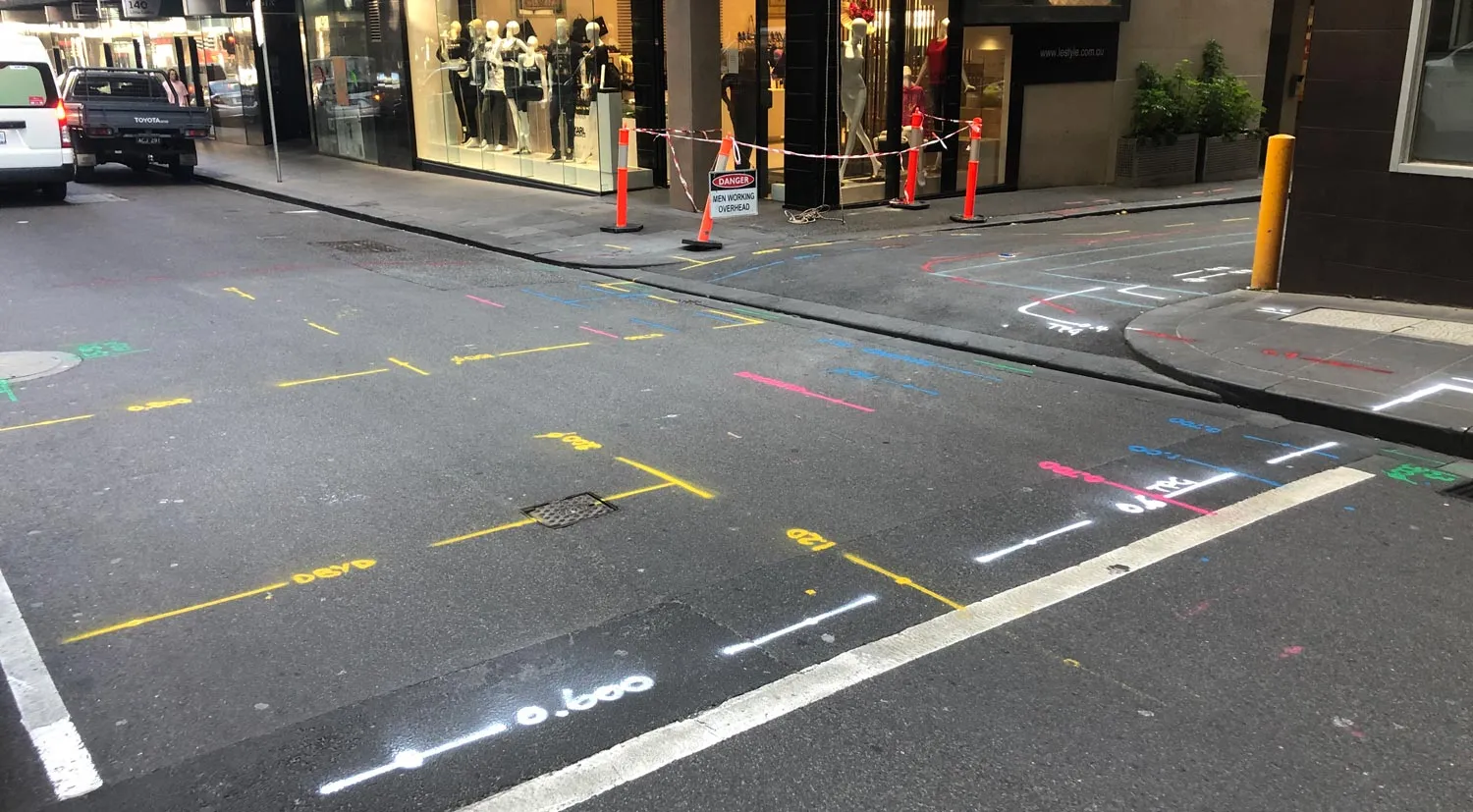 Locate marks in gas yellow, water blue, communications white and unknown-service pink sprayed across a city street works zone