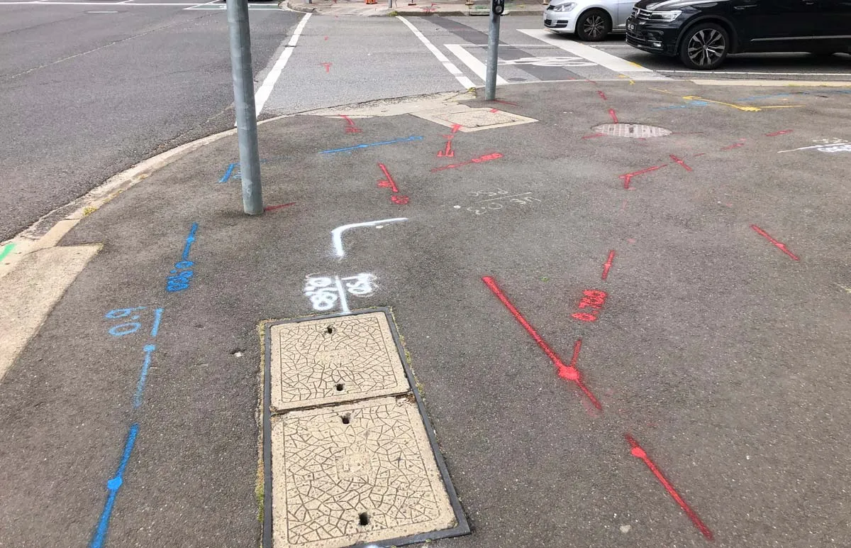 Blue water and pink unknown-service locate marks sprayed around a footpath pit
