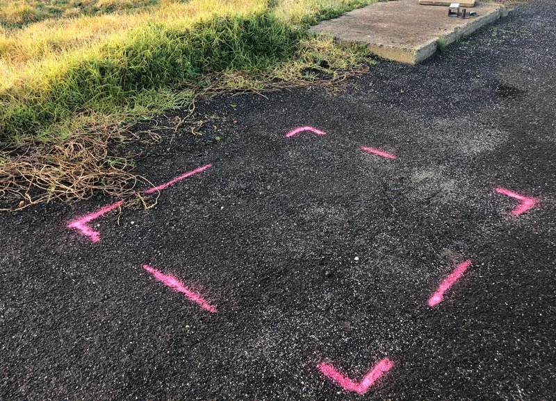A marked outrigger pad position on a verge beside a road