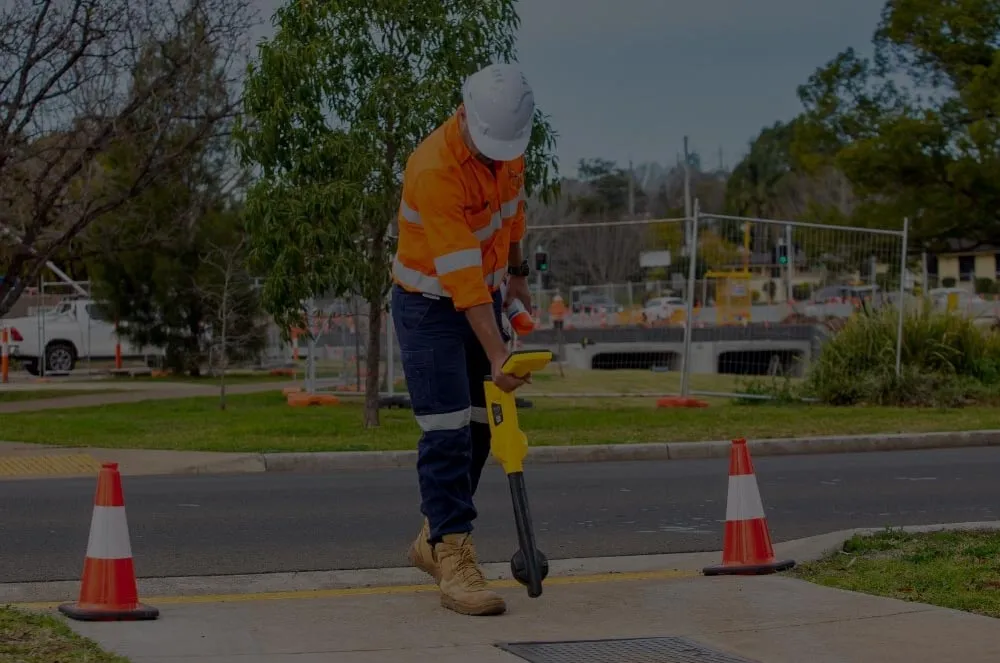 A locator in hi-vis tracing an underground service with a cable locator beside traffic cones