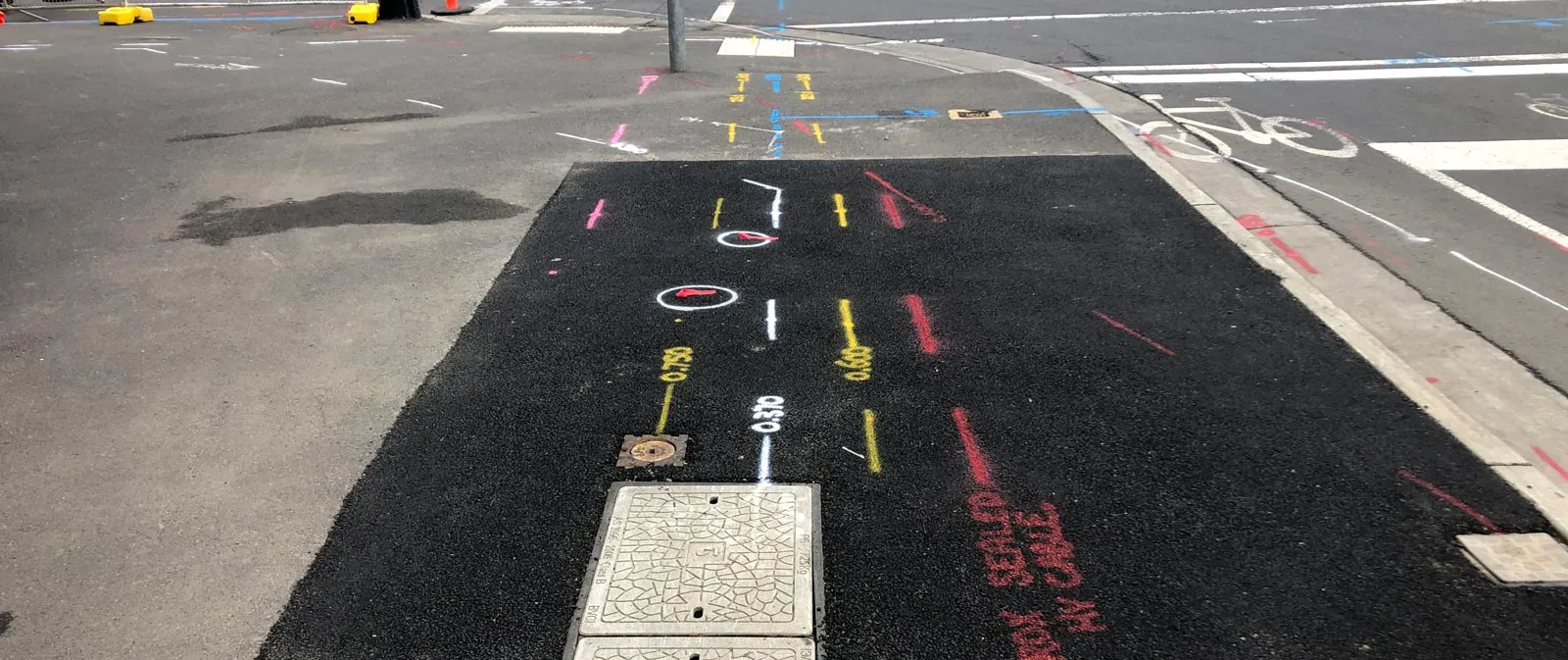 Freshly sealed asphalt with yellow, white and red locate marks and depth labels